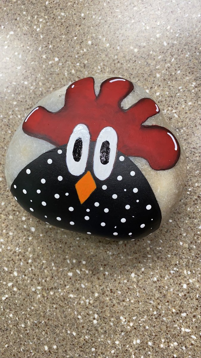Smooth river rock hand-painted with a cheerful chicken design — black body with white polka dots, red comb, and orange beak